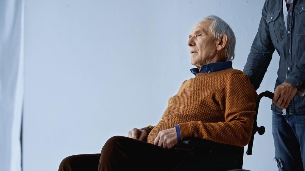 pensionista en silla de ruedas y hombre adulto sobre fondo gris - Foto, imagen