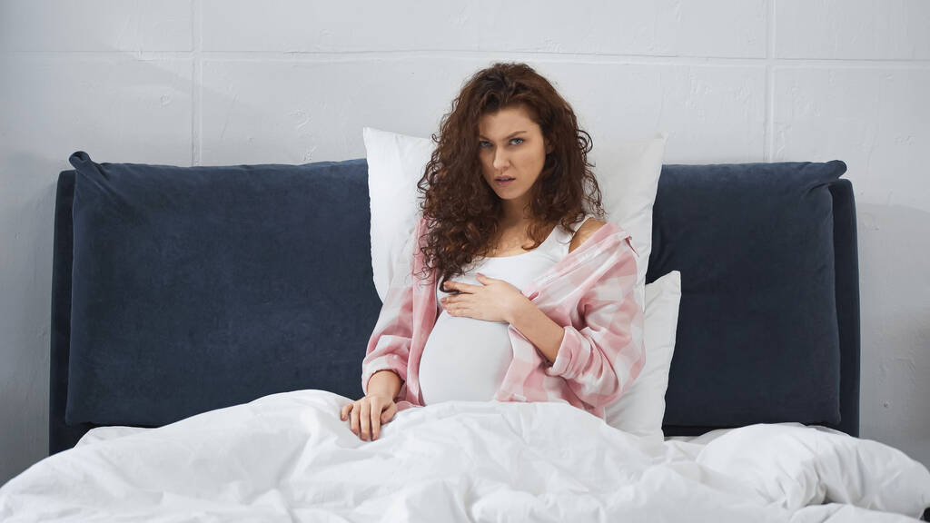 mujer embarazada tocando el vientre mientras está sentado en la cama  - Foto, imagen