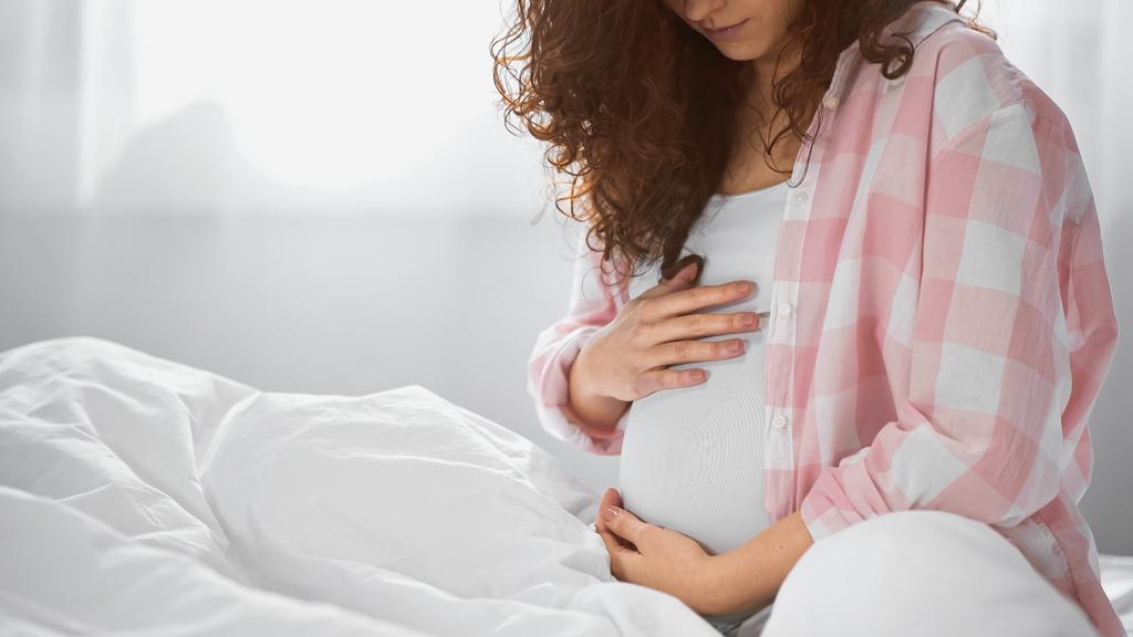 Teilansicht einer lockigen Schwangeren, die Bauch berührt  - Foto, Bild