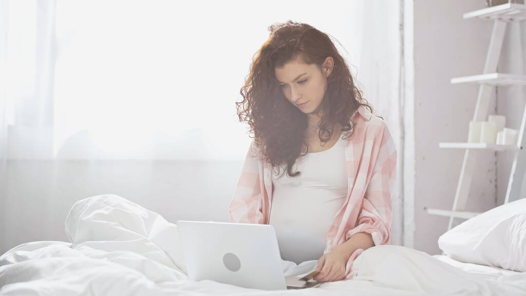 raskaana oleva nuori nainen käyttää kannettavaa tietokonetta sängyssä  - Valokuva, kuva