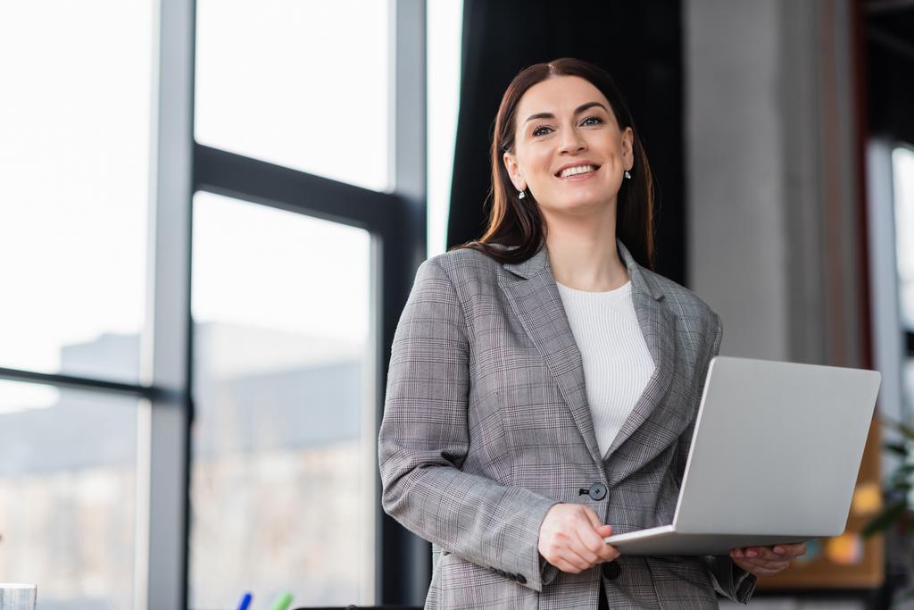 Businesswoman with laptop smiling at camera in office  - Photo, Image