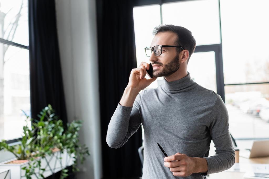 Üzletember tollat tart, miközben beszél okostelefonon az irodában  - Fotó, kép