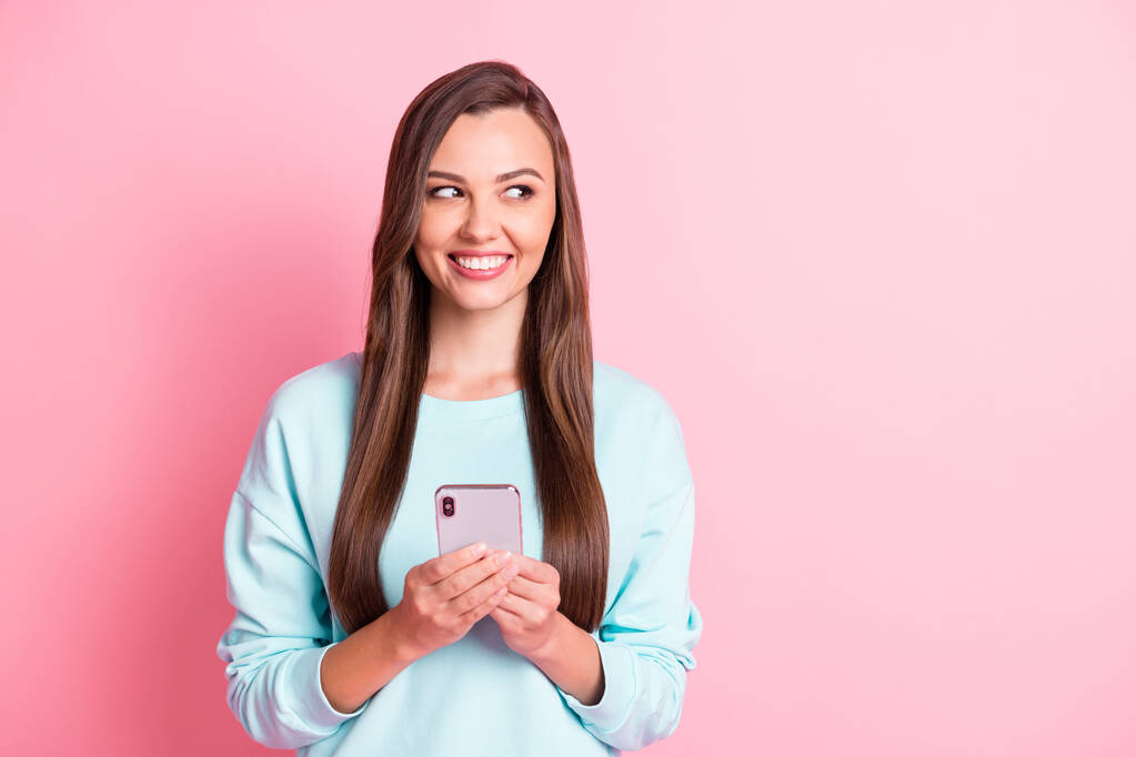 Foto von kreativen braunhaarige Frau suchen leeren Raum halten Telefon denken Nachricht isoliert auf rosa Hintergrund - Foto, Bild