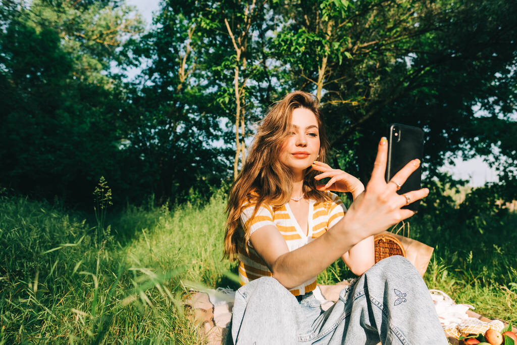 Jovem mulher alegre usando telefone celular fazendo selfie, no parque natural no piquenique, desfrutando de férias de verão. - Foto, Imagem