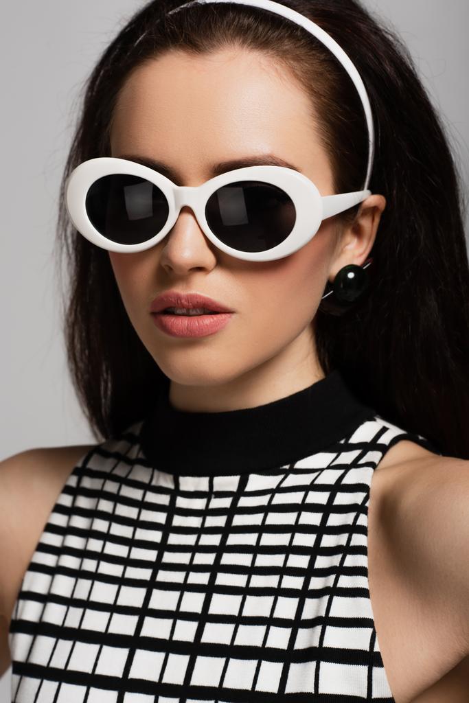trendy young model in sunglasses and headband isolated on grey  - Photo, Image