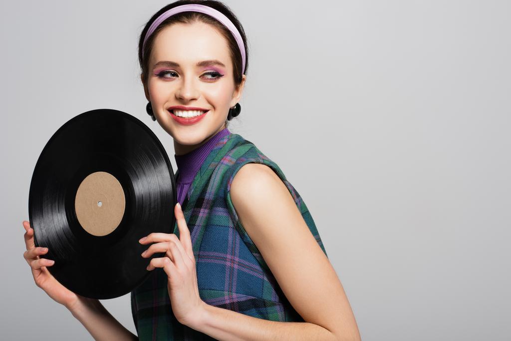 freudige Frau mit Stirnband hält Retro-Vinyl-Disc isoliert auf grau - Foto, Bild