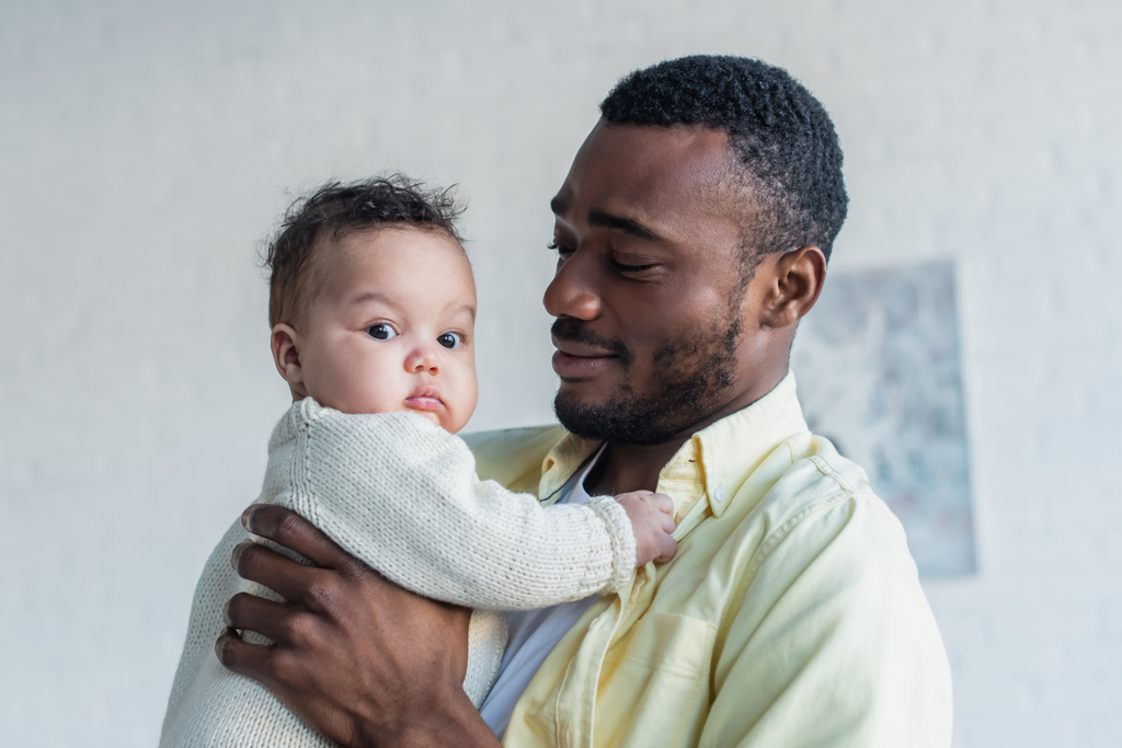 hombre afro-americano positivo sosteniendo a un bebé en casa - Foto, imagen