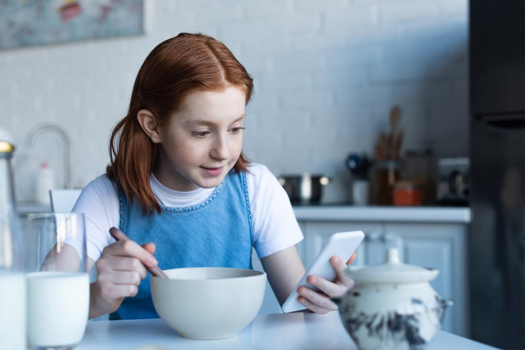 рыжеволосая девушка использует смартфон во время завтрака - Фото, изображение