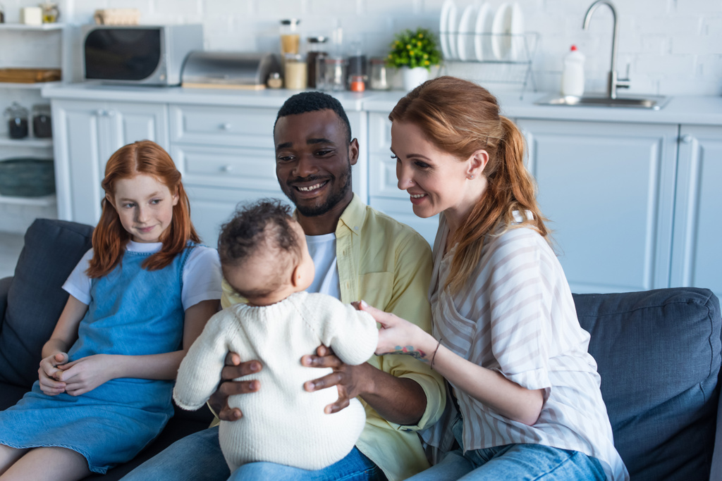 счастливый африканский американец держит младенца рядом с улыбающейся многонациональной семьей - Фото, изображение