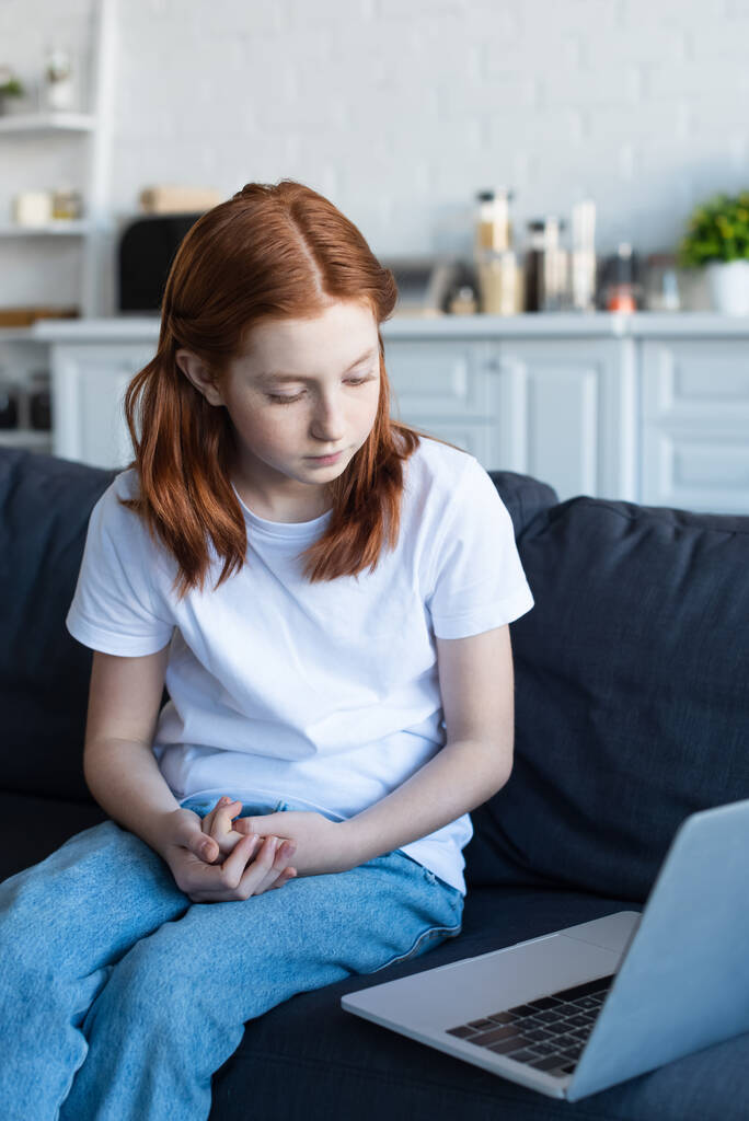 punapää tyttö katselee kannettavan tietokoneen sohvalla kotona - Valokuva, kuva