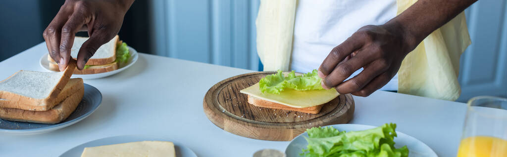 Afro-Amerikan erkeğinin peynirli, marullu ve pankartlı sandviç yapmasını kısmen görmek. - Fotoğraf, Görsel