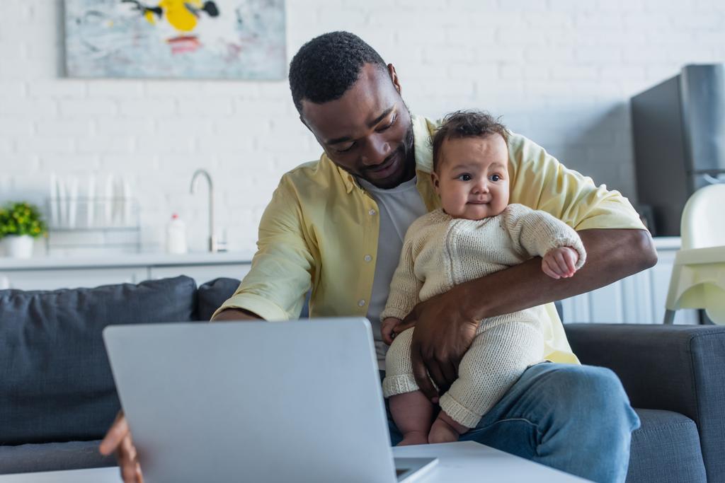 africano americano uomo seduto con neonato figlia vicino laptop - Foto, immagini