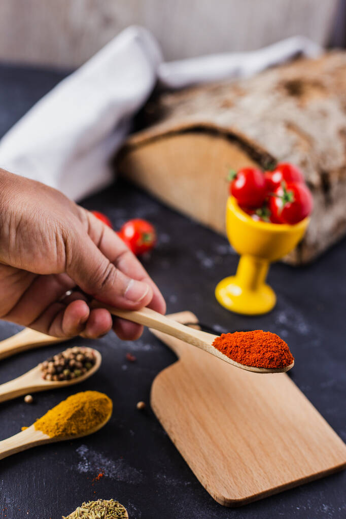 A hand holding a wooden spoon with spices and cherry tomatoes on the table - Photo, Image