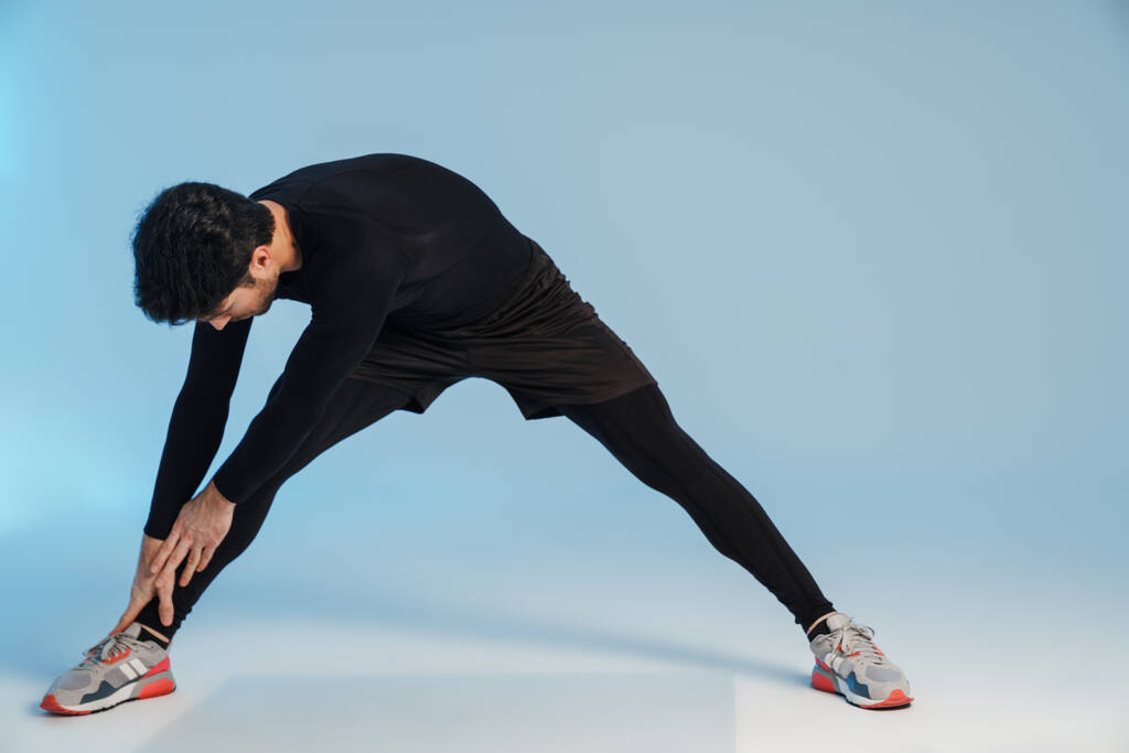Молодой спортсмен делает упражнения во время тренировки на голубом фоне - Фото, изображение