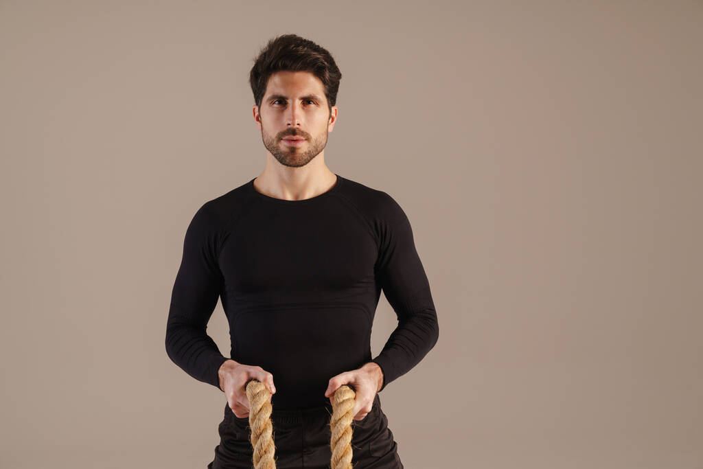 Esportista atlético bonito posando com cordas de batalha isoladas sobre fundo cinza - Foto, Imagem