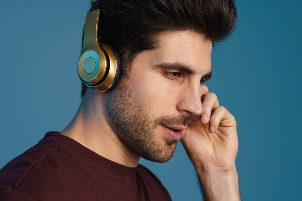 Χαρούμενος όμορφος άντρας ακούει μουσική με ασύρματα ακουστικά απομονωμένα σε μπλε φόντο - Φωτογραφία, εικόνα