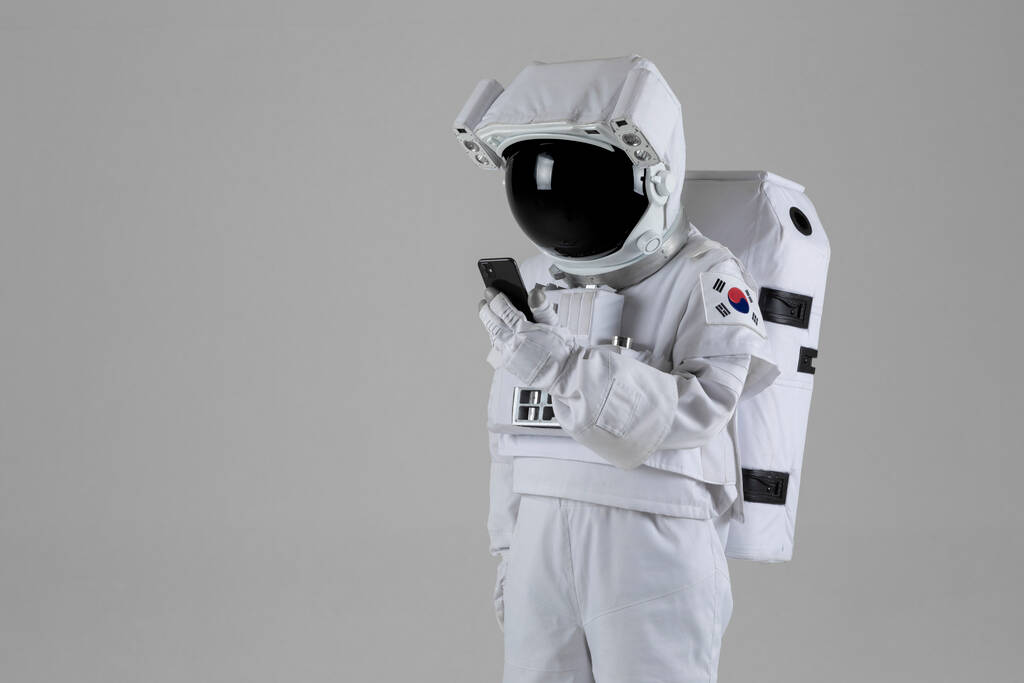 Astronauta mirando teléfono inteligente, fondo blanco - Foto, Imagen