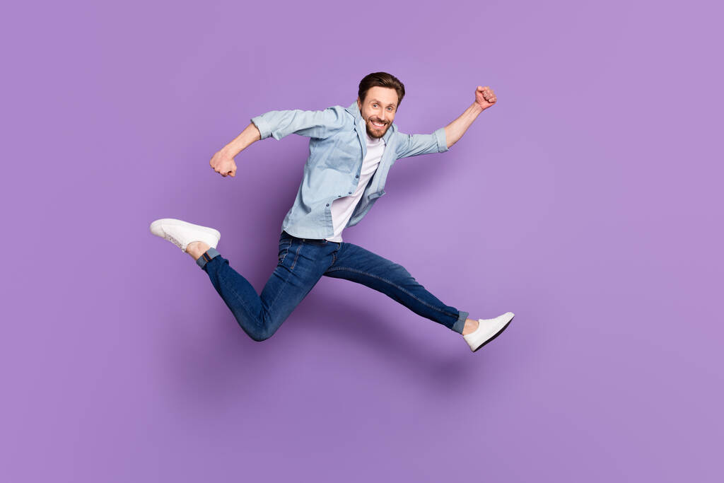 Full body profile side photo of attractive happy active man jump up run empty space isolated on purple color background - Photo, Image