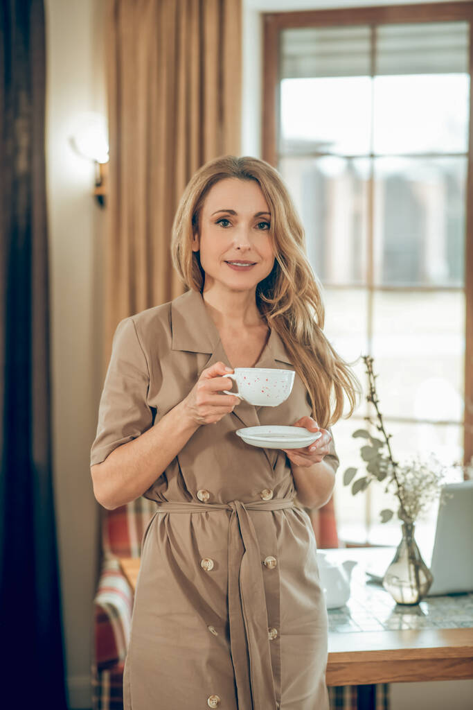 Довгошерста елегантна жінка має чай і виглядає задоволеною
 - Фото, зображення