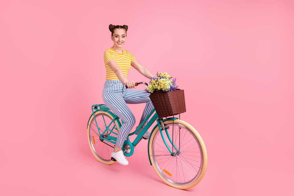 Teljes hossz profil fotó imádnivaló lány ülni kerékpár virágok kosárban elszigetelt rózsaszín háttér - Fotó, kép