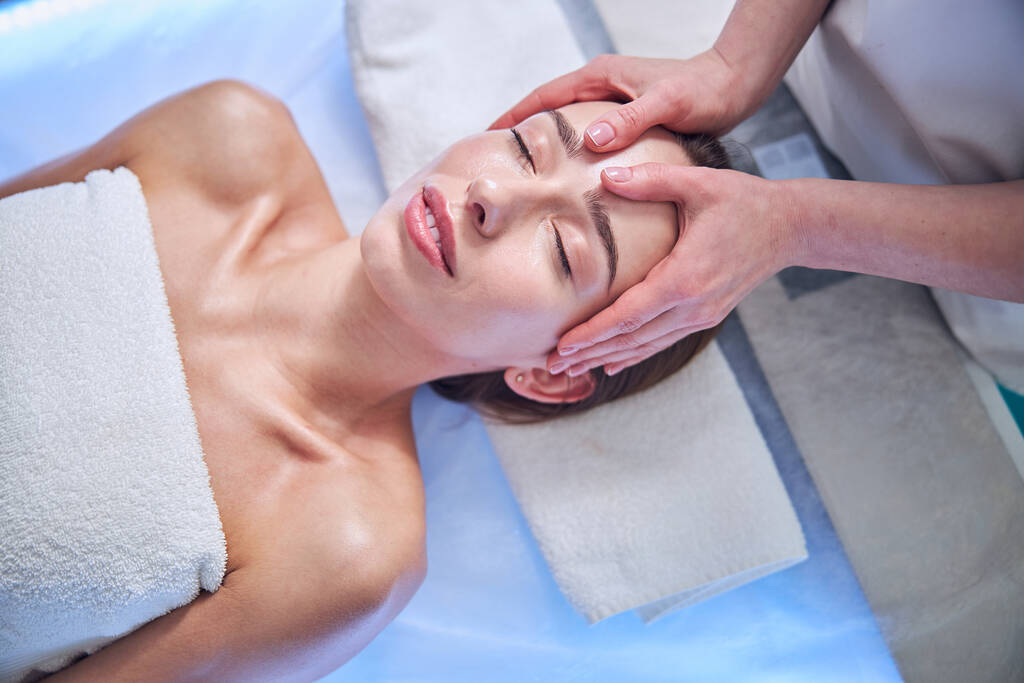 Belle femme élégante avec serviette sur son corps relaxant au spa massage du visage dans le salon de spa - Photo, image