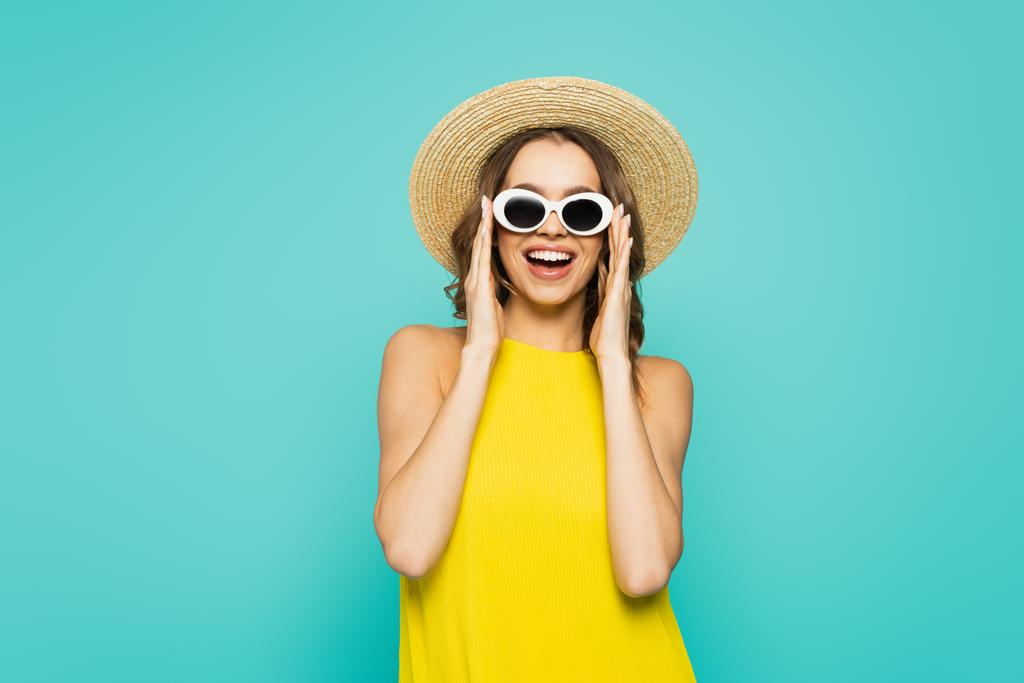 Positive woman in straw hat and sunglasses isolated on blue  - Photo, Image