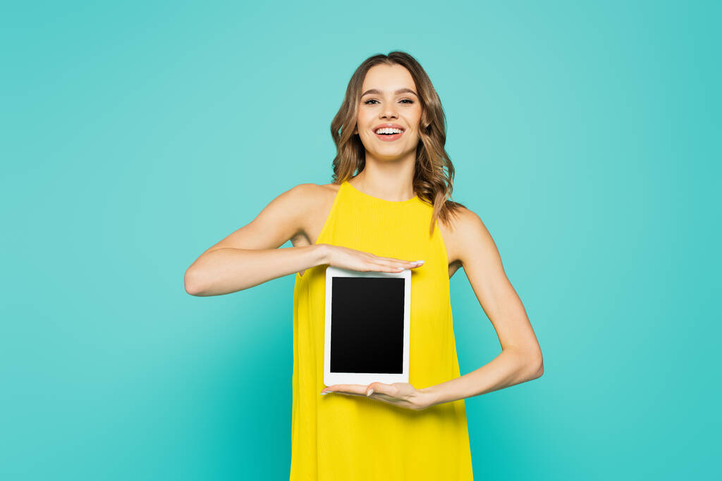 Donna sorridente che mostra tablet digitale con schermo vuoto isolato su blu  - Foto, immagini