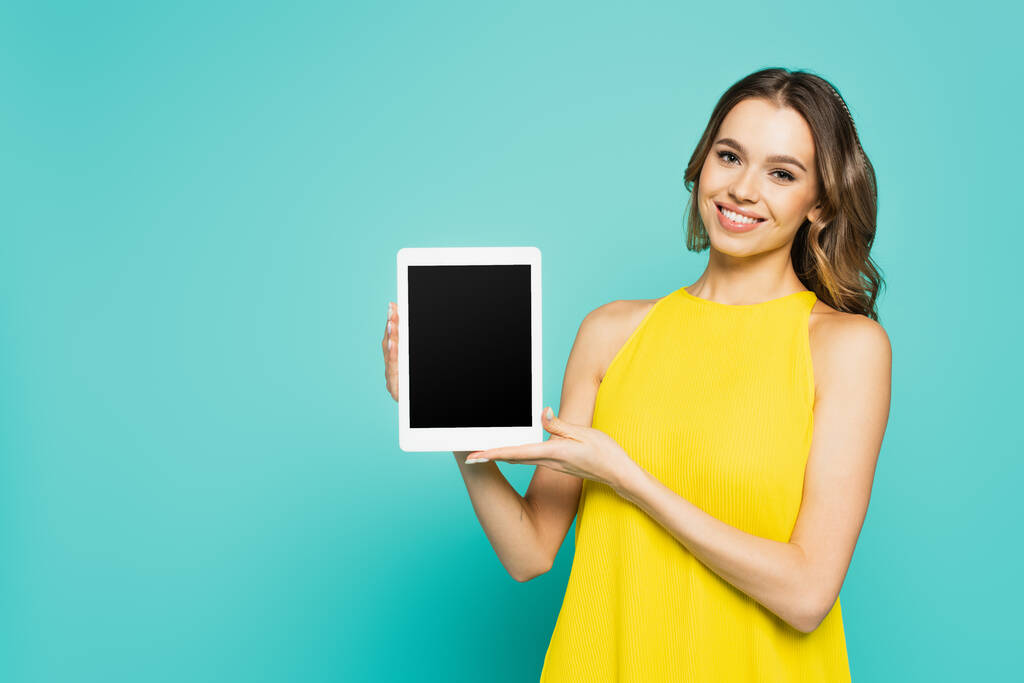 Sarı elbiseli pozitif kadın mavi ekranda boş ekranlı dijital tablet gösteriyor.  - Fotoğraf, Görsel