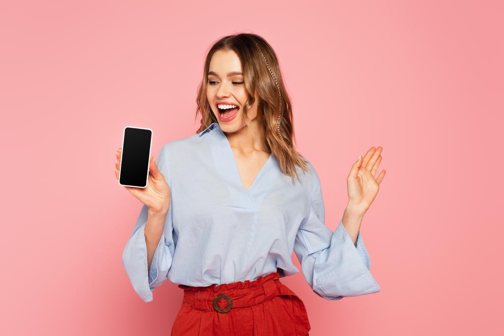 Χαρούμενη γυναίκα δείχνει smartphone με λευκή οθόνη που απομονώνονται σε ροζ  - Φωτογραφία, εικόνα