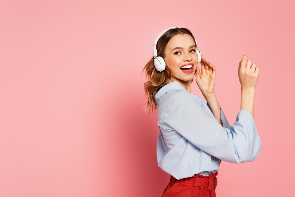 Positive Frau mit Kopfhörern, die auf rosa Hintergrund wegschaut  - Foto, Bild