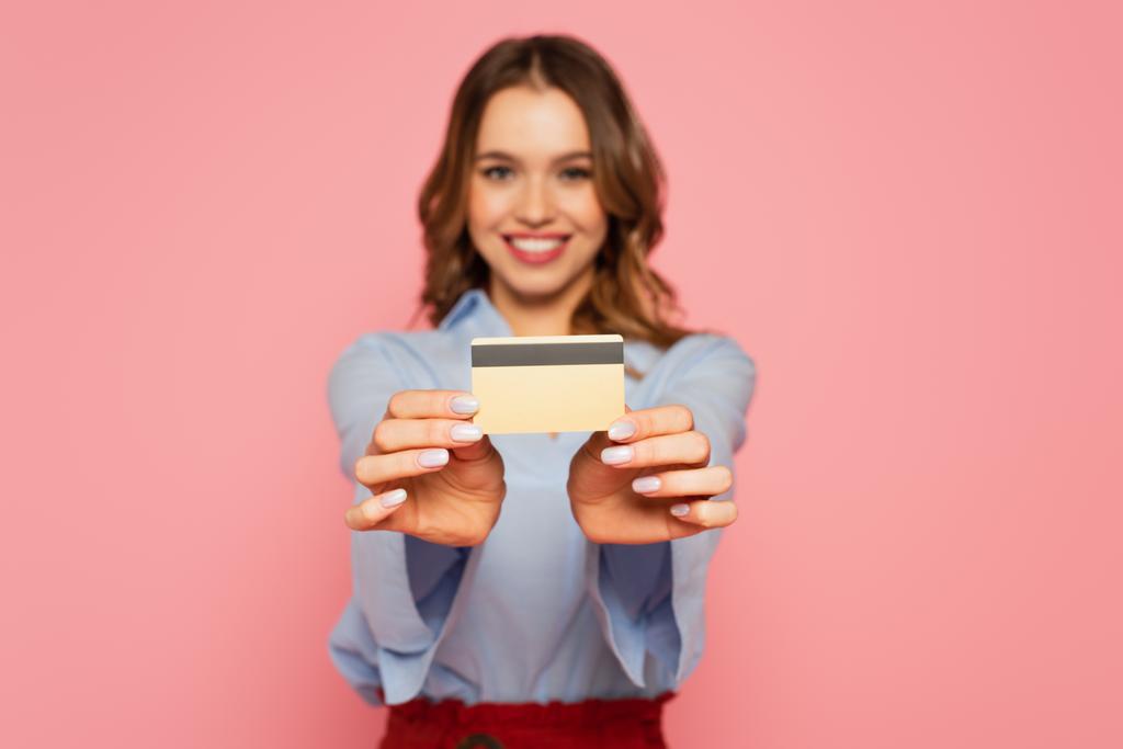 Кредитная карта в руках улыбающейся женщины на размытом фоне изолированы на розовый  - Фото, изображение