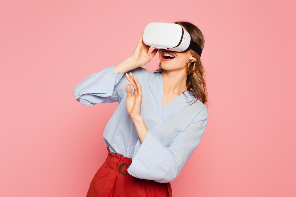 Улыбающаяся женщина с помощью наушников виртуальной реальности, изолированных на розовый  - Фото, изображение