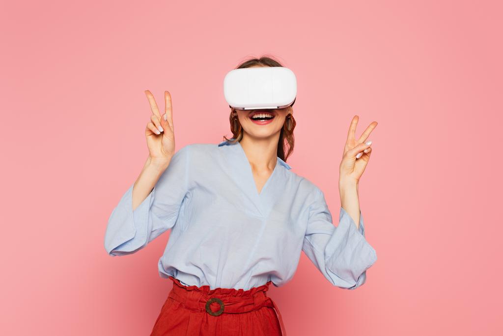 Smiling woman in vr headset showing peace signs isolated on pink  - Photo, Image