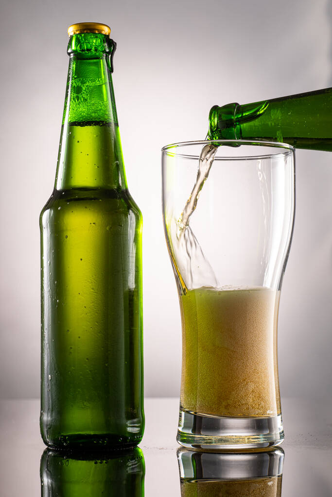 Bira bardağı, köpük ve yanında bira olan yeşil şeffaf şişe. - Fotoğraf, Görsel