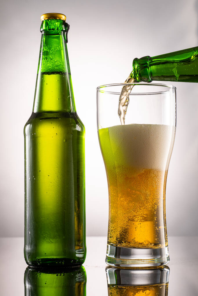 Pivní sklo a pěna a zelená průhledná láhev s pivem vedle - Fotografie, Obrázek
