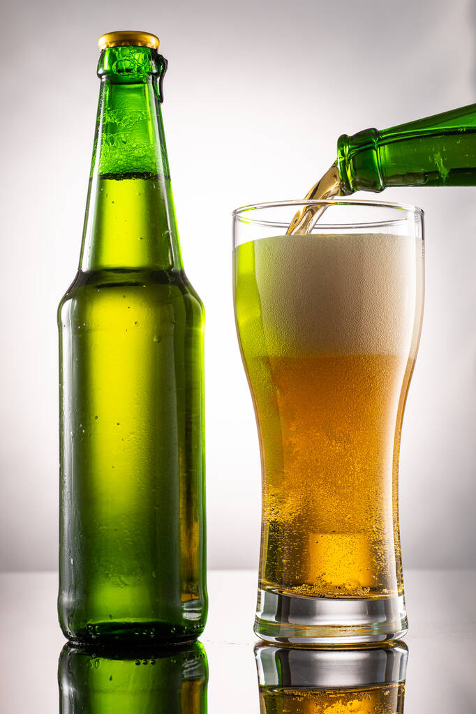 Beer glass and foam and green transparent bottle with beer beside - Foto, afbeelding