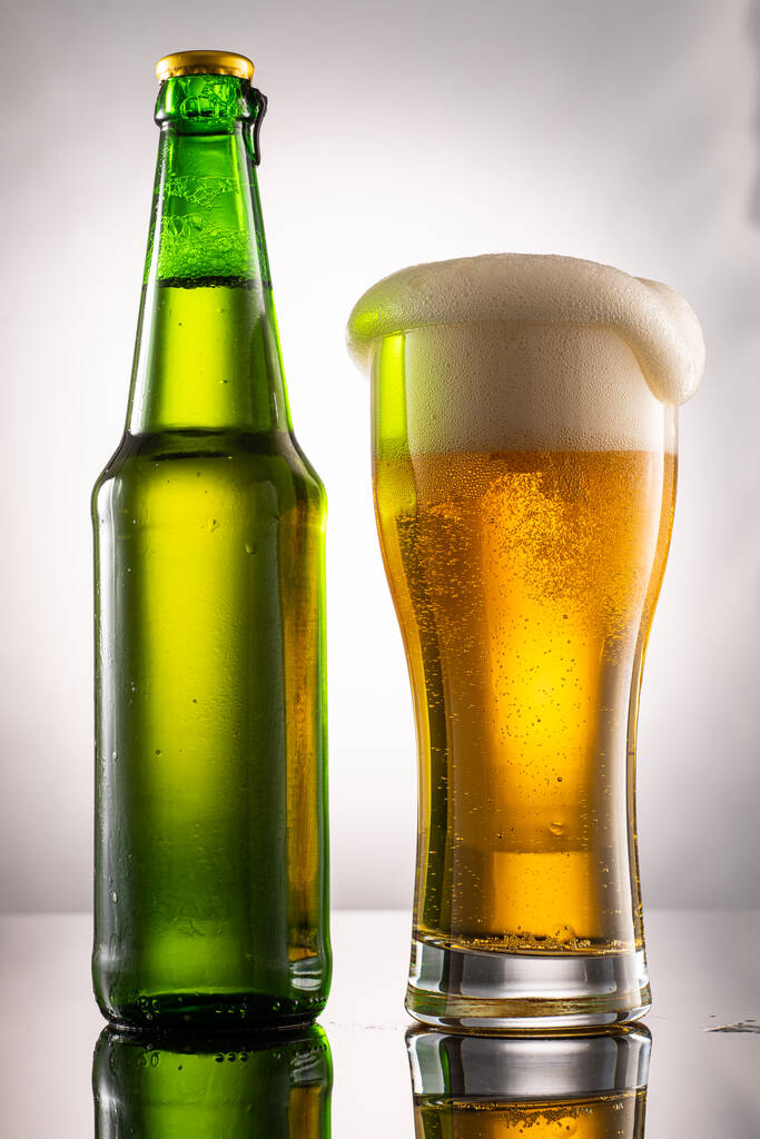 Bierglas und Schaumstoff und grüne transparente Flasche mit Bier daneben - Foto, Bild