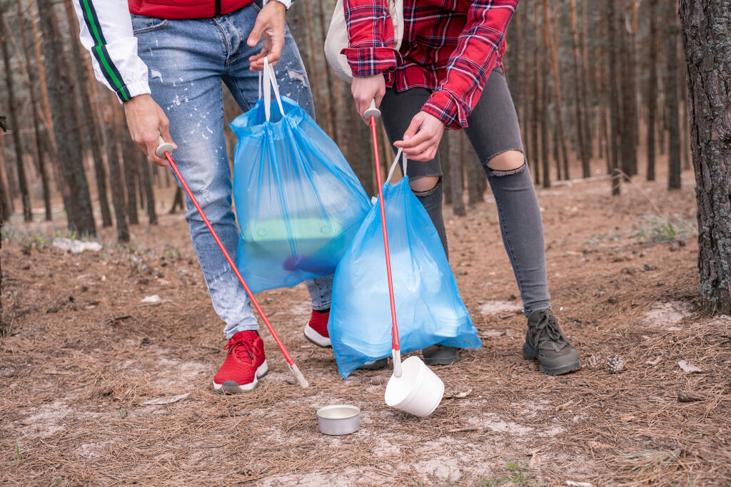 vista cortada de casal com sacos de lixo pegando lixo com ferramentas grabber na floresta  - Foto, Imagem