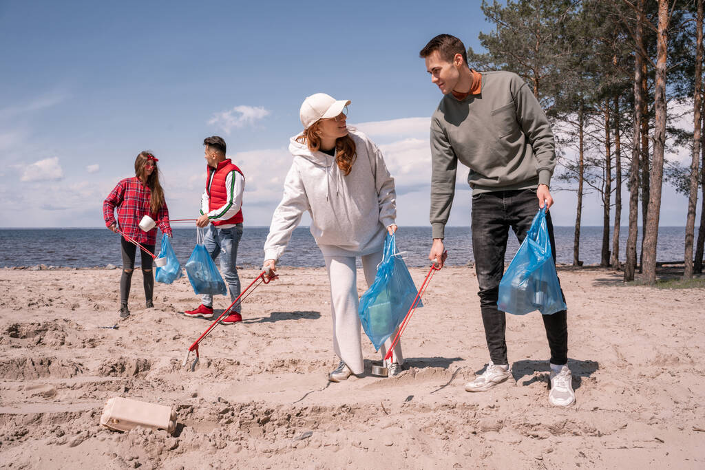 Glückliche Gruppe freiwilliger Helfer mit Müllsäcken, die mit Greifwerkzeugen Müll aufheben  - Foto, Bild