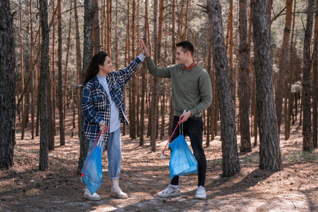 Ormanda çöp torbalarıyla çöpleri toplarken çöp torbaları olan mutlu çiftler beşlik çakıyor.  - Fotoğraf, Görsel