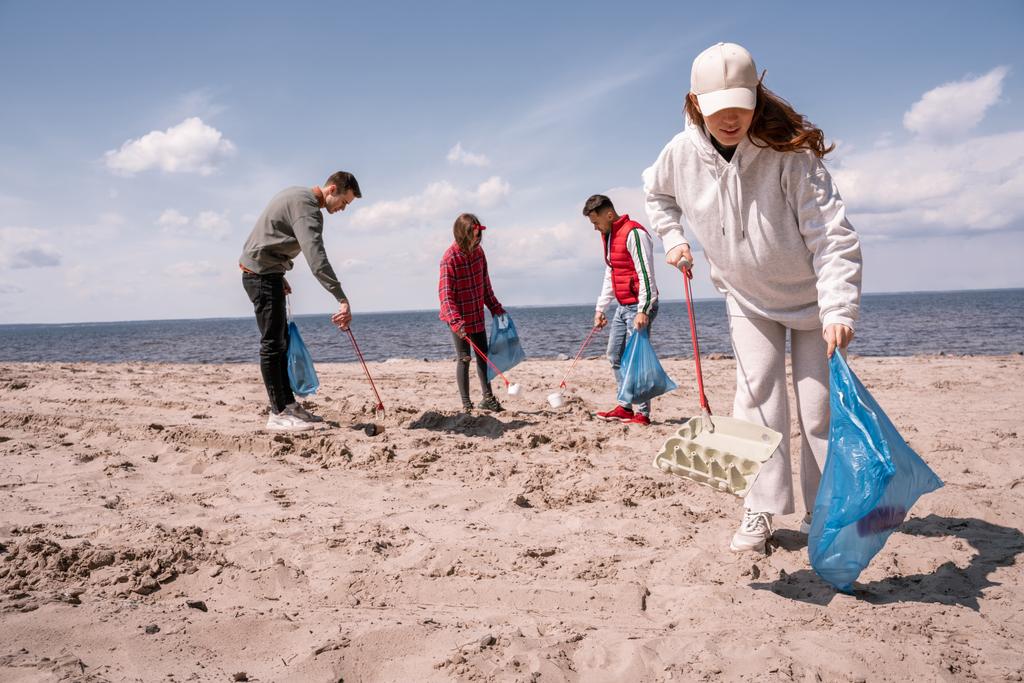 ゴミ袋を持ったボランティアグループが砂の上でゴミを拾い  - 写真・画像