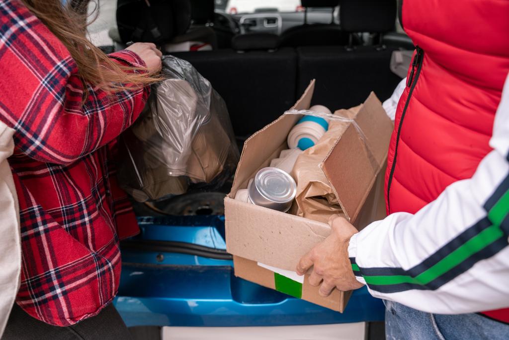 oříznutý pohled na ženu držící pytel na odpadky, zatímco muž stojící s kartonovou krabicí v blízkosti auta  - Fotografie, Obrázek