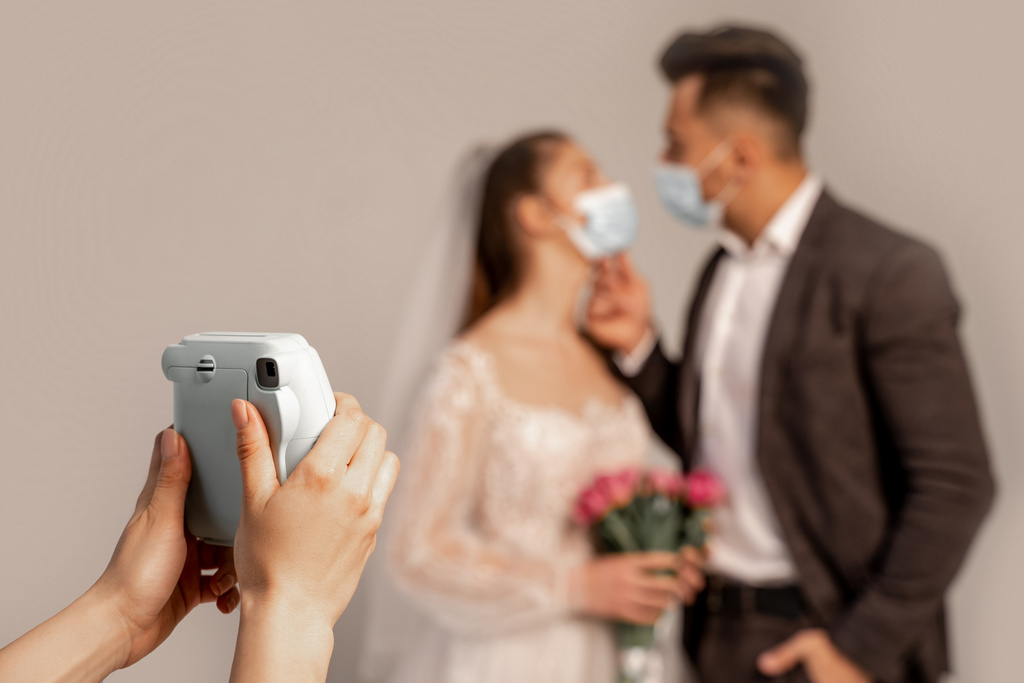 woman taking photo of blurred newlyweds in medical masks isolated on grey - Foto, Imagem