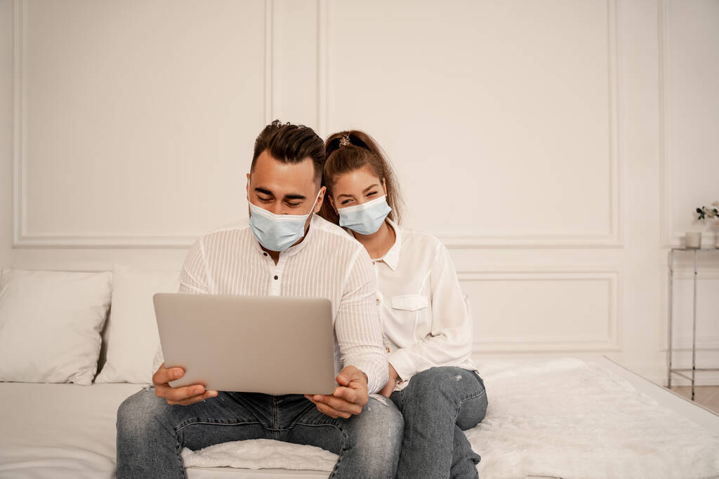 couple in safety masks watching movie on laptop during quarantine at home - Photo, Image