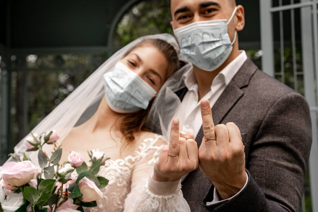 couple of newlyweds in safety masks showing wedding rings at camera - Foto, Imagem