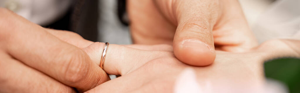 частичный вид человека, надевающего обручальное кольцо на палец невесты, знамя - Фото, изображение