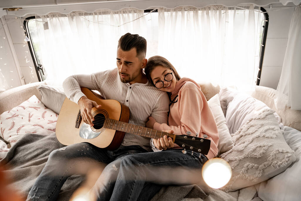happy woman hugging boyfriend playing guitar in camper - Zdjęcie, obraz