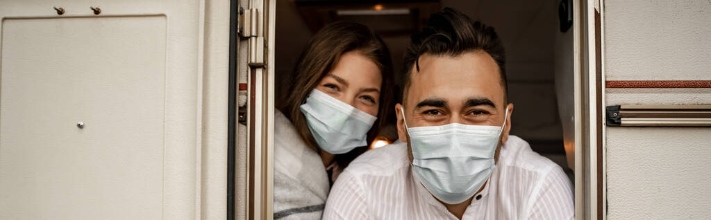 молодая пара в защитных масках, выглядывающая из трейлера, баннера - Фото, изображение
