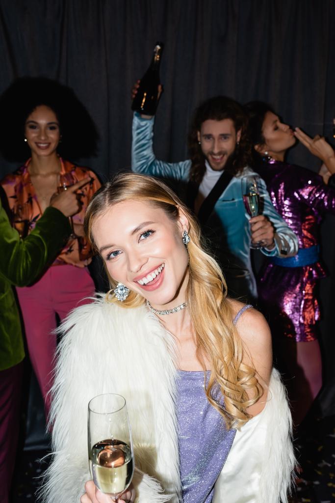 souriant jeune femme blonde adulte avec verre de champagne sur la fête avec des amis interracial sur fond gris - Photo, image