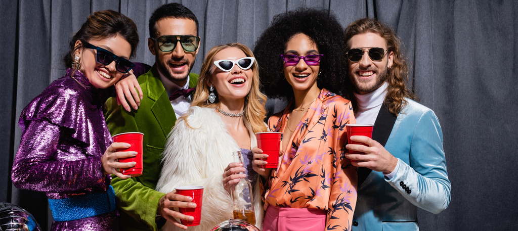 smiling interracial friends in sunglasses standing on grey background, banner - Photo, Image